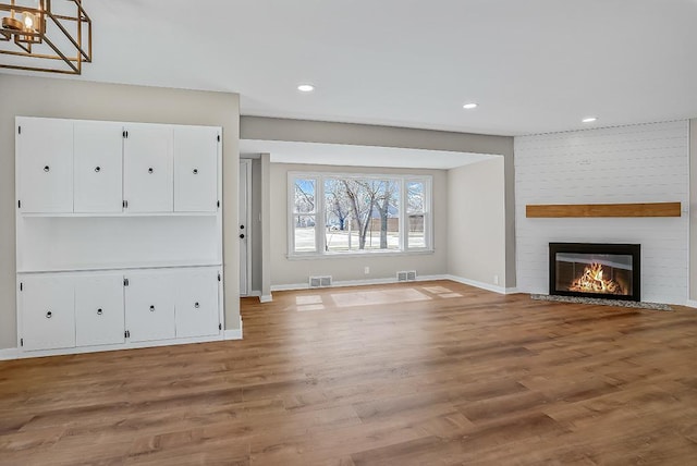 unfurnished living room with visible vents, baseboards, a large fireplace, and light wood-style floors