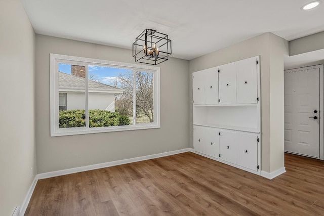 unfurnished dining area with a notable chandelier, a baseboard heating unit, baseboards, and wood finished floors