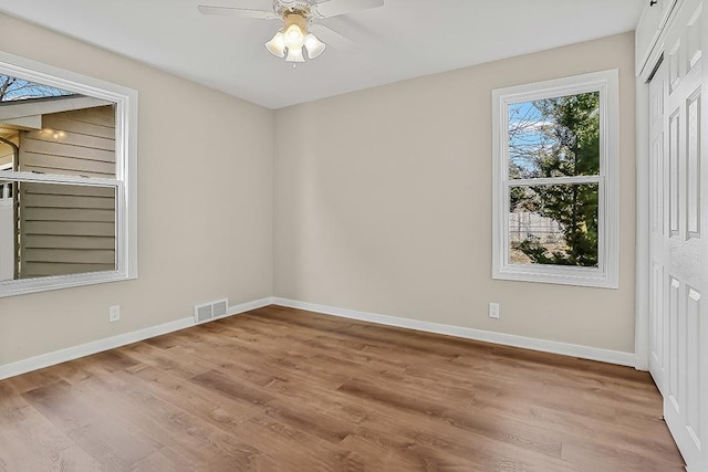 empty room featuring a ceiling fan, baseboards, visible vents, and light wood finished floors