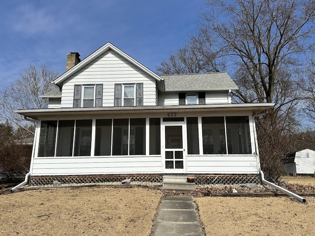 view of front of house with entry steps, a sunroom, a chimney, and roof with shingles