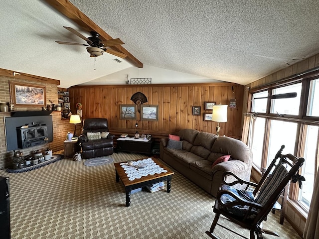 living area with carpet, vaulted ceiling with beams, a wood stove, wooden walls, and a textured ceiling