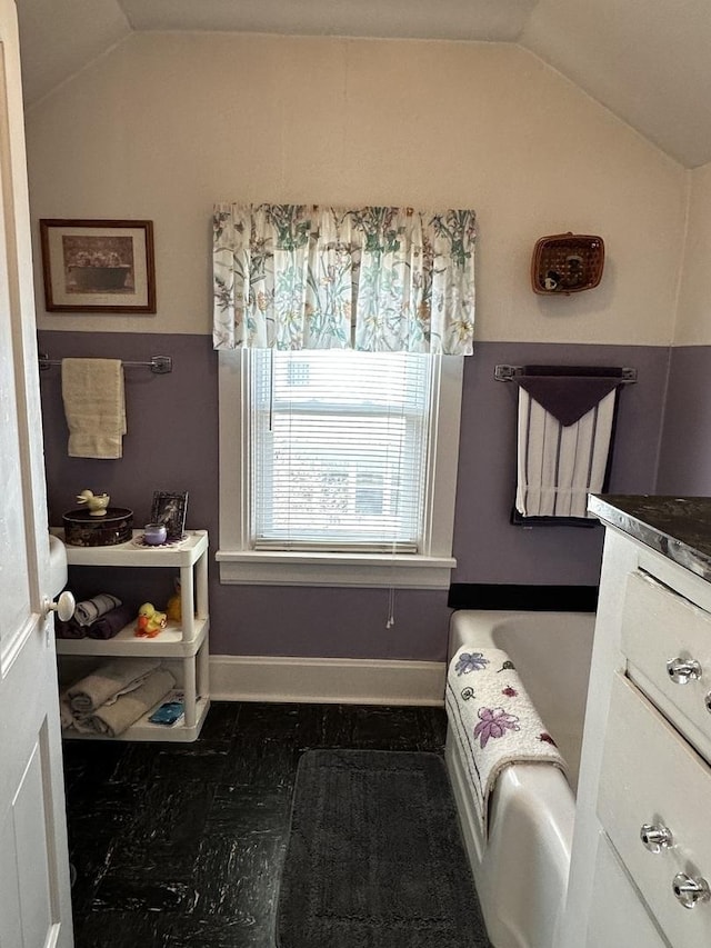 bathroom featuring lofted ceiling, vanity, baseboards, and a bathing tub