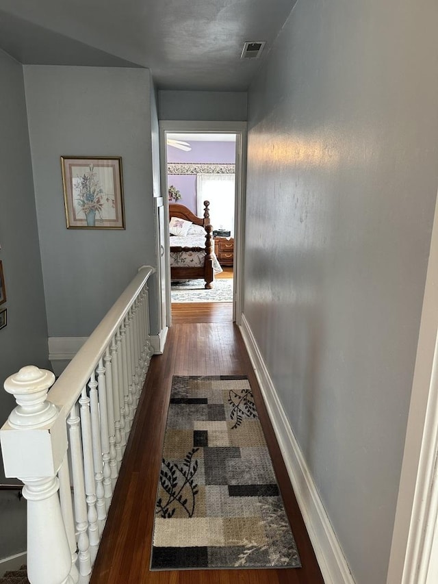 corridor featuring visible vents, dark wood-style flooring, an upstairs landing, and baseboards