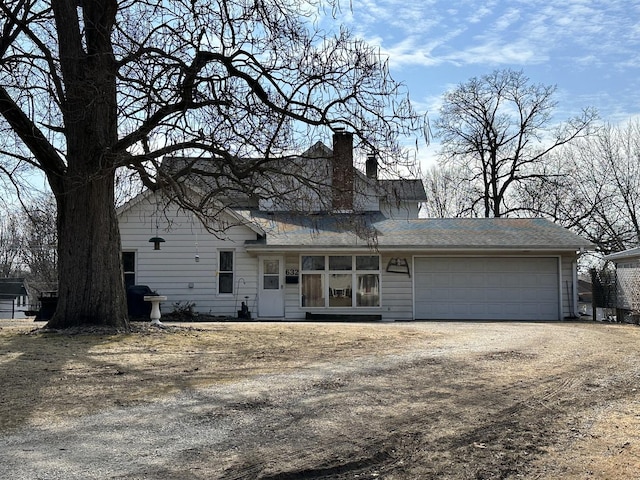 view of front facade featuring driveway, a chimney, and an attached garage