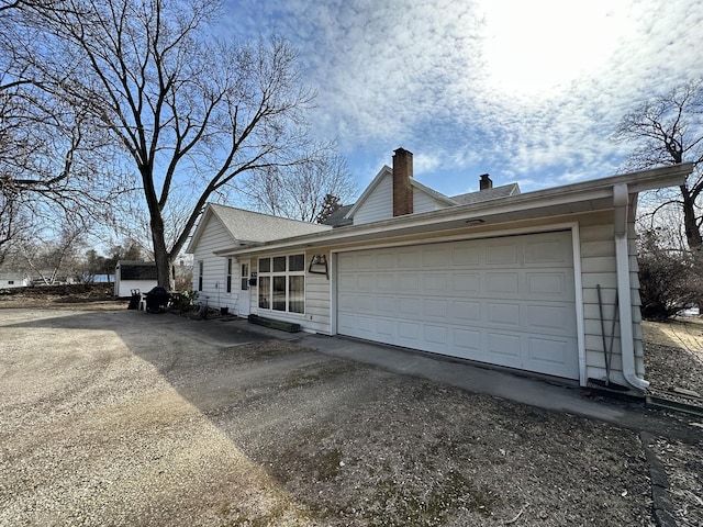 view of front facade with an attached garage, a chimney, and aphalt driveway