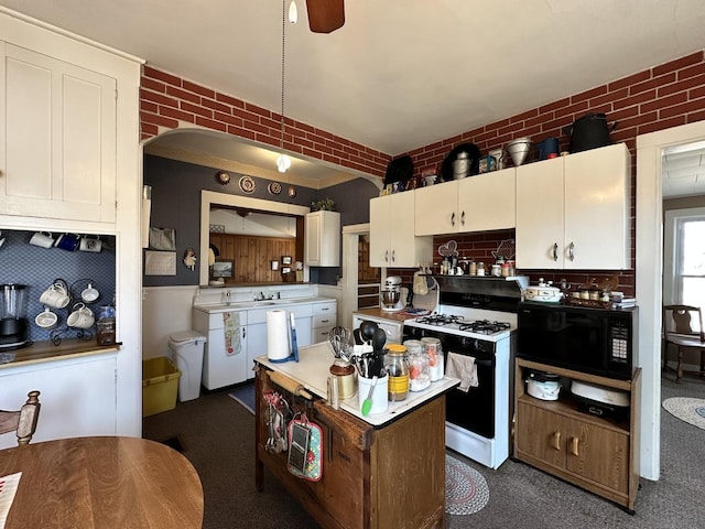 kitchen featuring black microwave, brick wall, and range with gas stovetop