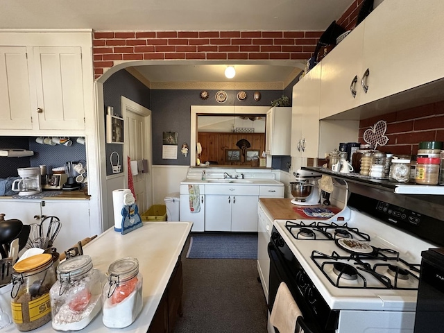 kitchen with arched walkways, white gas stove, light countertops, and white cabinetry