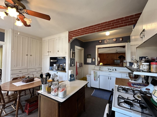 kitchen with arched walkways, white gas stove, light countertops, white cabinetry, and ceiling fan