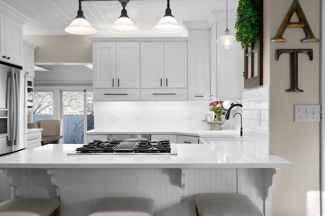 kitchen with stovetop with downdraft, ornamental molding, white cabinets, a sink, and a kitchen bar