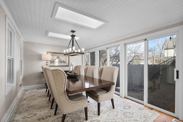 dining space featuring a skylight, light wood finished floors, baseboards, wooden ceiling, and a chandelier