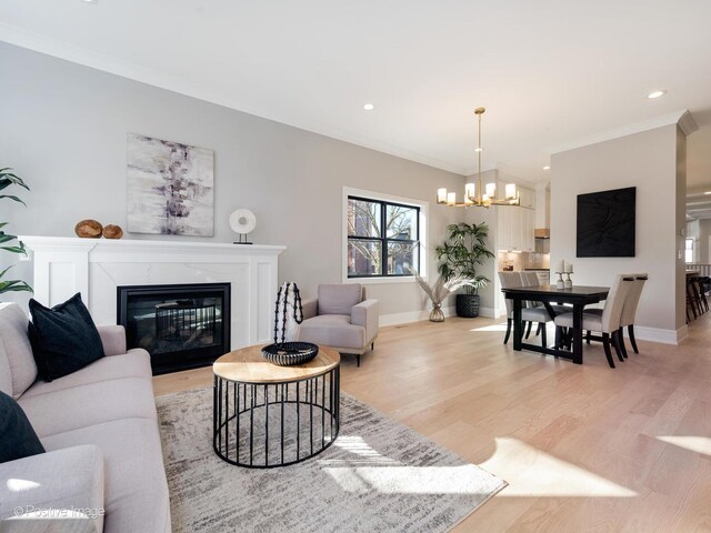 living room with baseboards, an inviting chandelier, crown molding, light wood-type flooring, and a high end fireplace