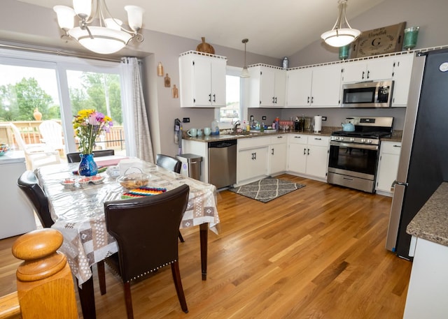 kitchen with white cabinets, lofted ceiling, stainless steel appliances, light wood-type flooring, and a notable chandelier