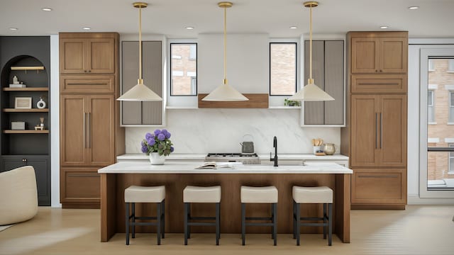 kitchen with a center island with sink, light countertops, a sink, and decorative light fixtures