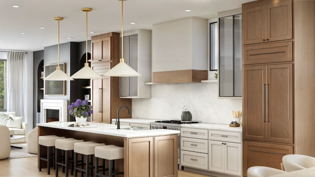 kitchen with tasteful backsplash, light countertops, a kitchen island with sink, a sink, and wall chimney range hood