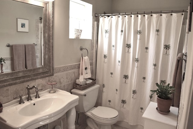 bathroom featuring a wainscoted wall, a sink, curtained shower, tile walls, and toilet