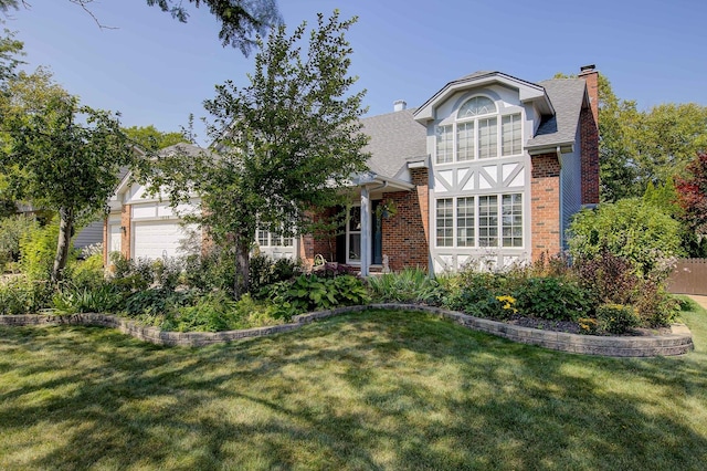 english style home with a garage, a front yard, a chimney, and brick siding