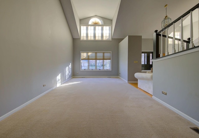 unfurnished living room with high vaulted ceiling, carpet floors, visible vents, baseboards, and stairway