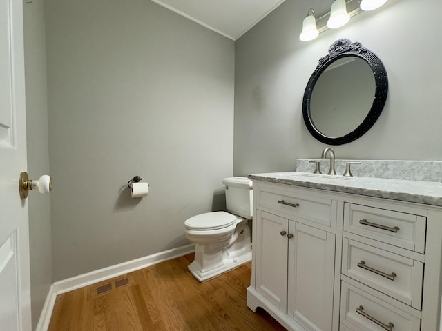 half bath with toilet, wood finished floors, vanity, visible vents, and baseboards