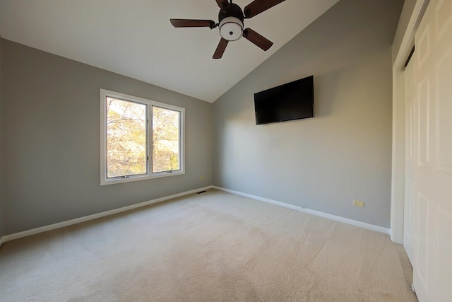 carpeted spare room featuring lofted ceiling, ceiling fan, and baseboards