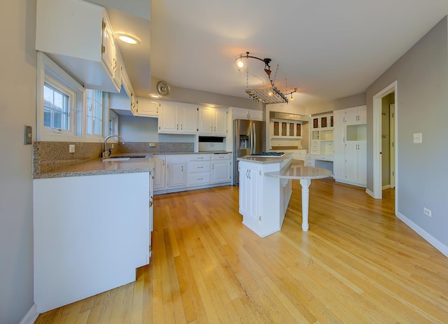 kitchen featuring a breakfast bar, stainless steel refrigerator with ice dispenser, white cabinetry, a kitchen island, and a sink