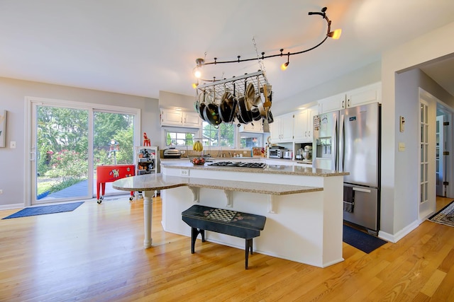 kitchen with appliances with stainless steel finishes, white cabinets, a kitchen island, light wood-type flooring, and a kitchen bar