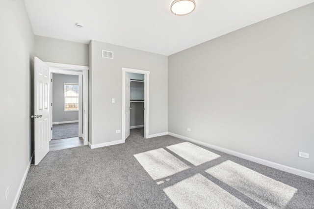 unfurnished bedroom with carpet floors, a walk in closet, visible vents, and baseboards