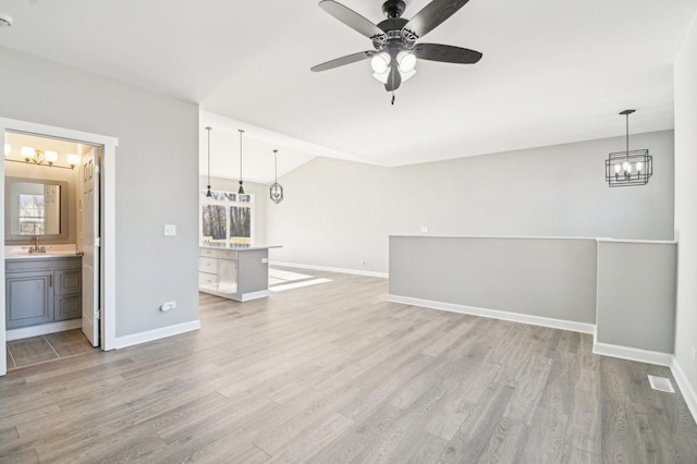 unfurnished living room featuring ceiling fan with notable chandelier, light wood-style flooring, and baseboards