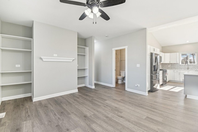 unfurnished living room featuring light wood-style flooring, a ceiling fan, a sink, vaulted ceiling, and baseboards