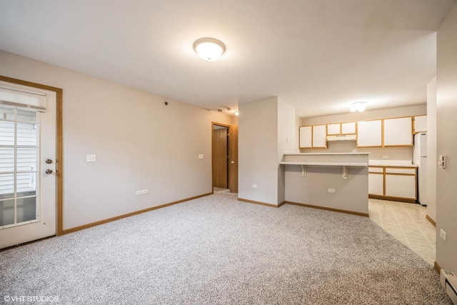 unfurnished living room with a baseboard heating unit, baseboards, and light colored carpet