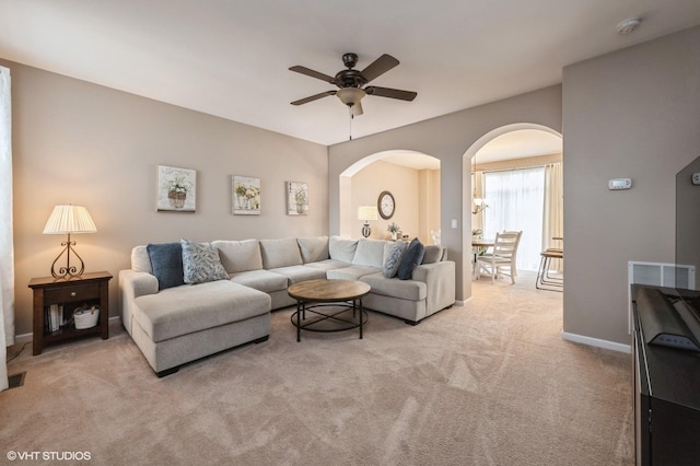 carpeted living room with arched walkways, ceiling fan, and baseboards