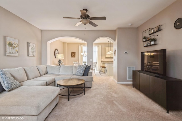 living area with ceiling fan, arched walkways, light colored carpet, visible vents, and baseboards