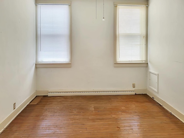 spare room with a baseboard heating unit, a healthy amount of sunlight, and hardwood / wood-style floors