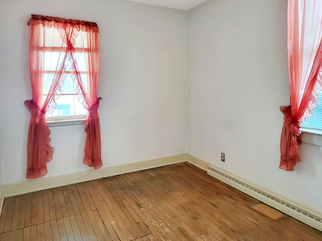 unfurnished room featuring baseboard heating, wood-type flooring, and baseboards