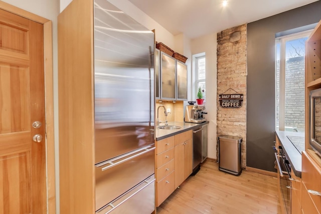 kitchen with stainless steel appliances, backsplash, a sink, and light wood-style flooring