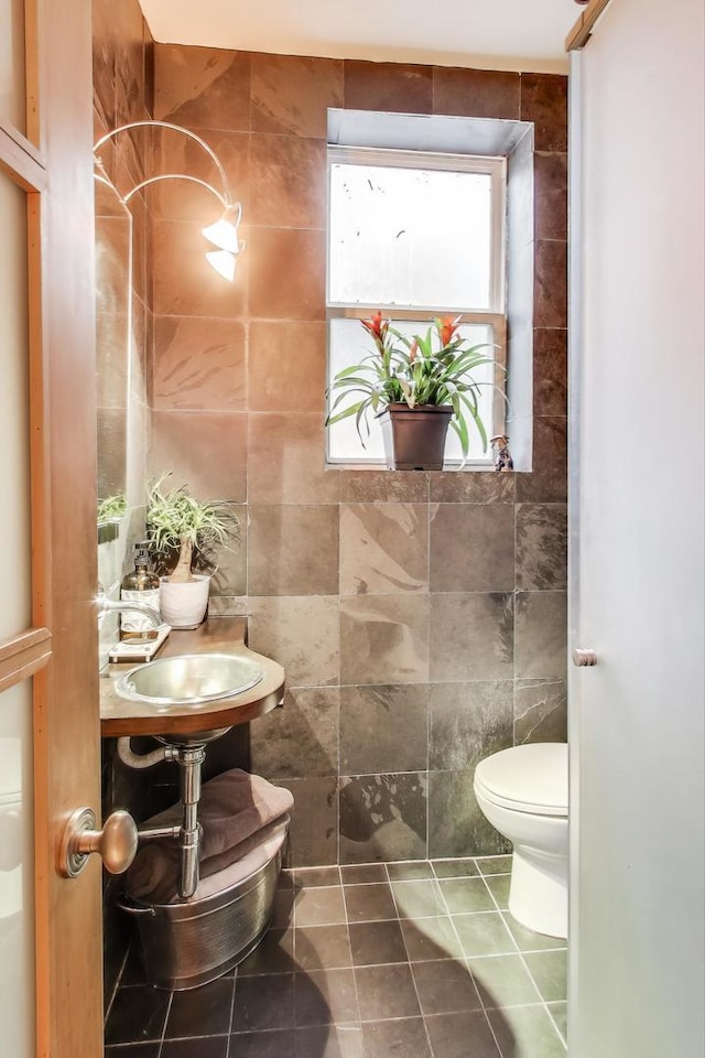 bathroom with toilet, tile patterned flooring, and tile walls