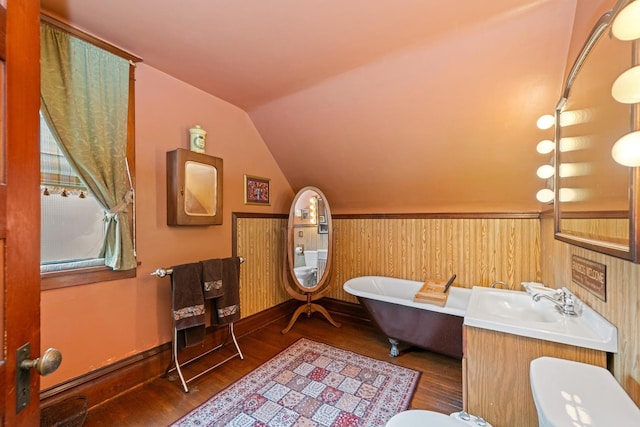 bathroom featuring vaulted ceiling, toilet, a freestanding bath, a sink, and wood finished floors
