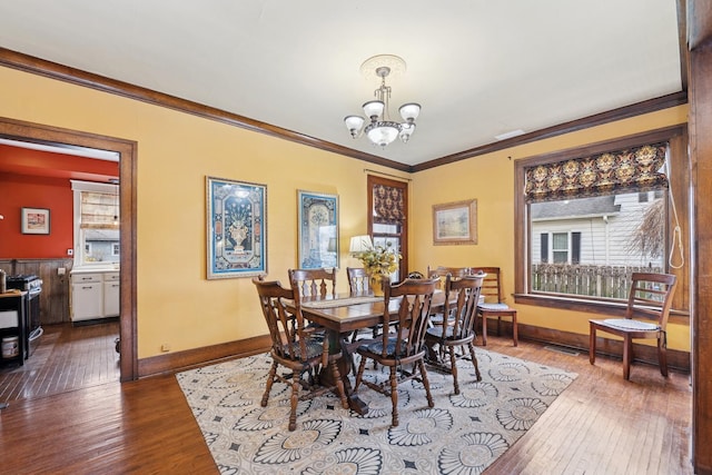 dining area featuring a chandelier, wood-type flooring, baseboards, and ornamental molding