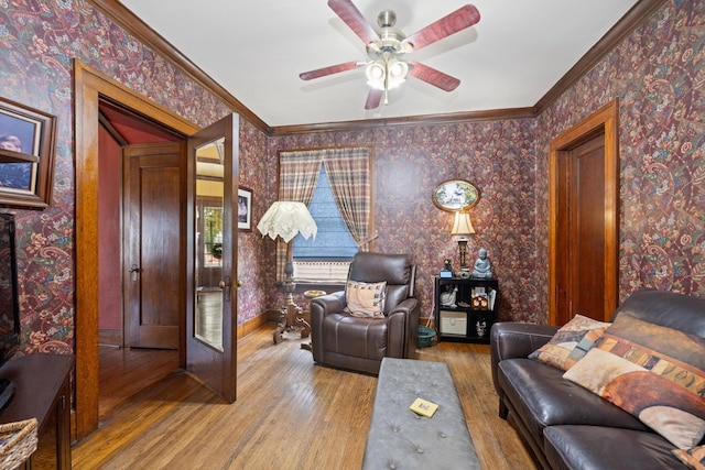 living room featuring ceiling fan, wallpapered walls, crown molding, and wood finished floors
