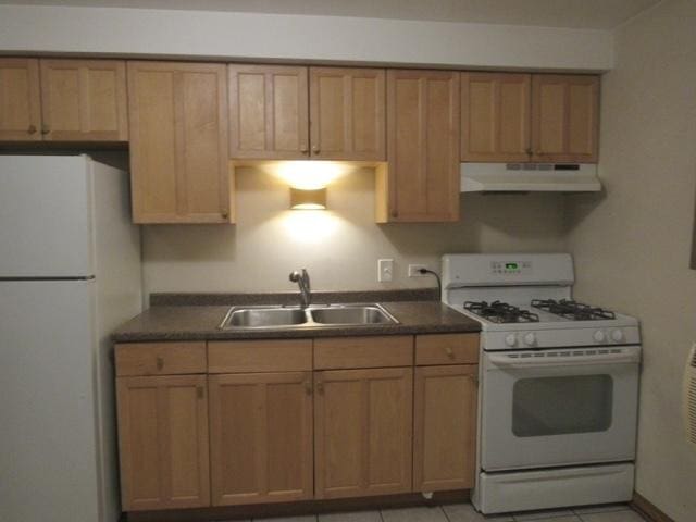 kitchen featuring dark countertops, brown cabinetry, a sink, white appliances, and under cabinet range hood