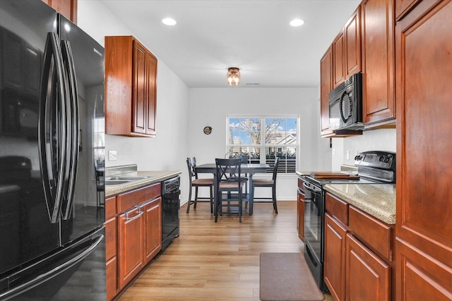 kitchen with baseboards, light wood finished floors, recessed lighting, a sink, and black appliances