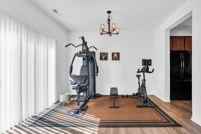 exercise area featuring an inviting chandelier, wood finished floors, visible vents, and baseboards