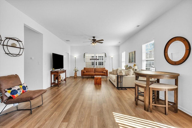 living room with light wood-type flooring, baseboards, visible vents, and ceiling fan