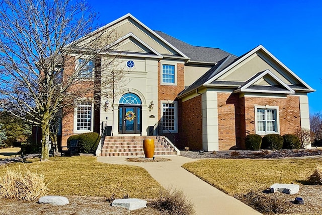 traditional-style house with roof with shingles, a front yard, and brick siding