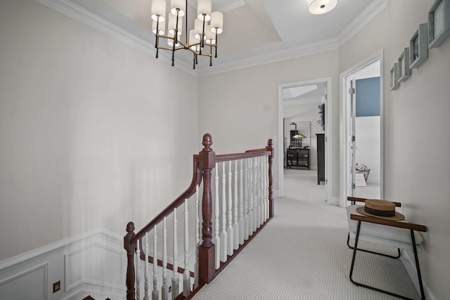 hall with a decorative wall, carpet floors, an upstairs landing, ornamental molding, and an inviting chandelier