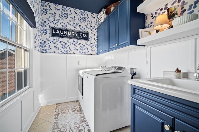 laundry room with cabinet space, wallpapered walls, wainscoting, washer and dryer, and a sink