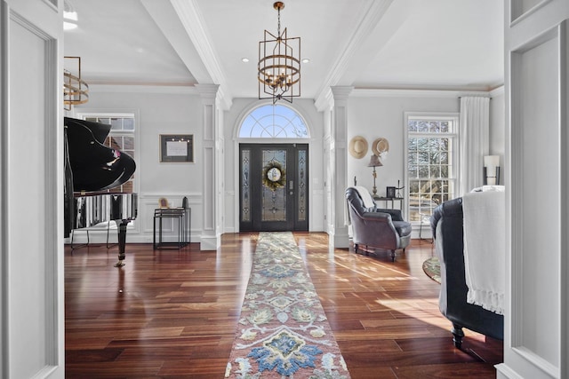 foyer with a notable chandelier, ornamental molding, wood finished floors, and ornate columns