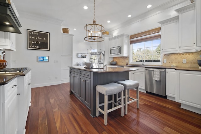 kitchen featuring white cabinets, dark countertops, ornamental molding, stainless steel appliances, and wall chimney range hood