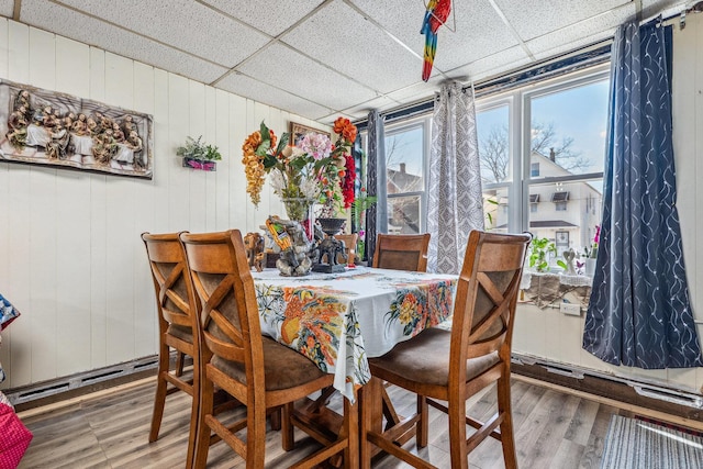 dining room featuring a baseboard heating unit, wood finished floors, and a paneled ceiling