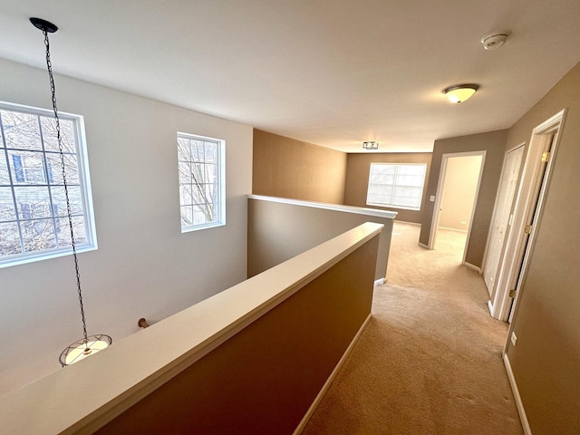 hall with baseboards, an upstairs landing, and light colored carpet