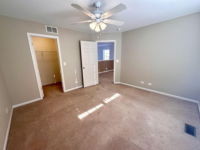 unfurnished bedroom with baseboards, visible vents, a walk in closet, and carpet flooring